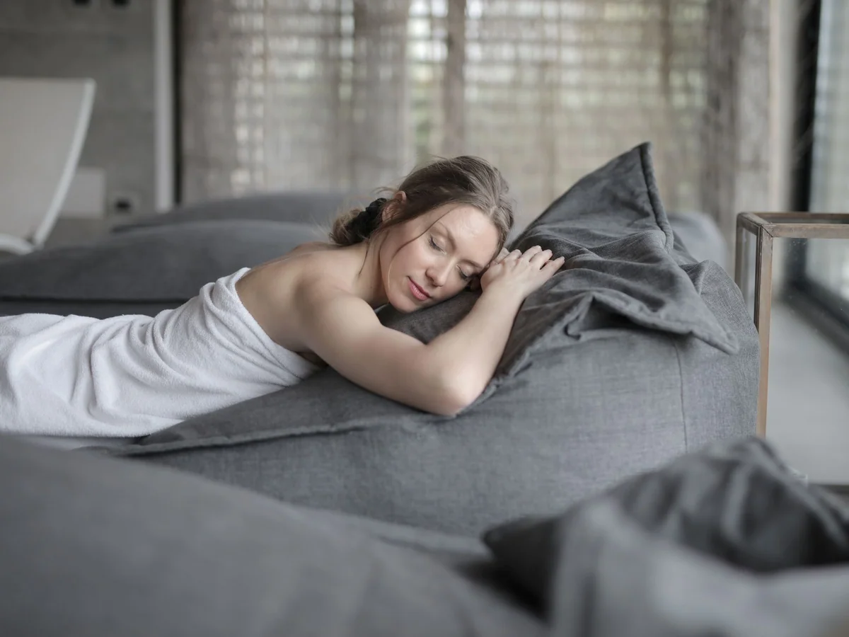 Woman resting briefly on a sofa while keeping a glass of water nearby